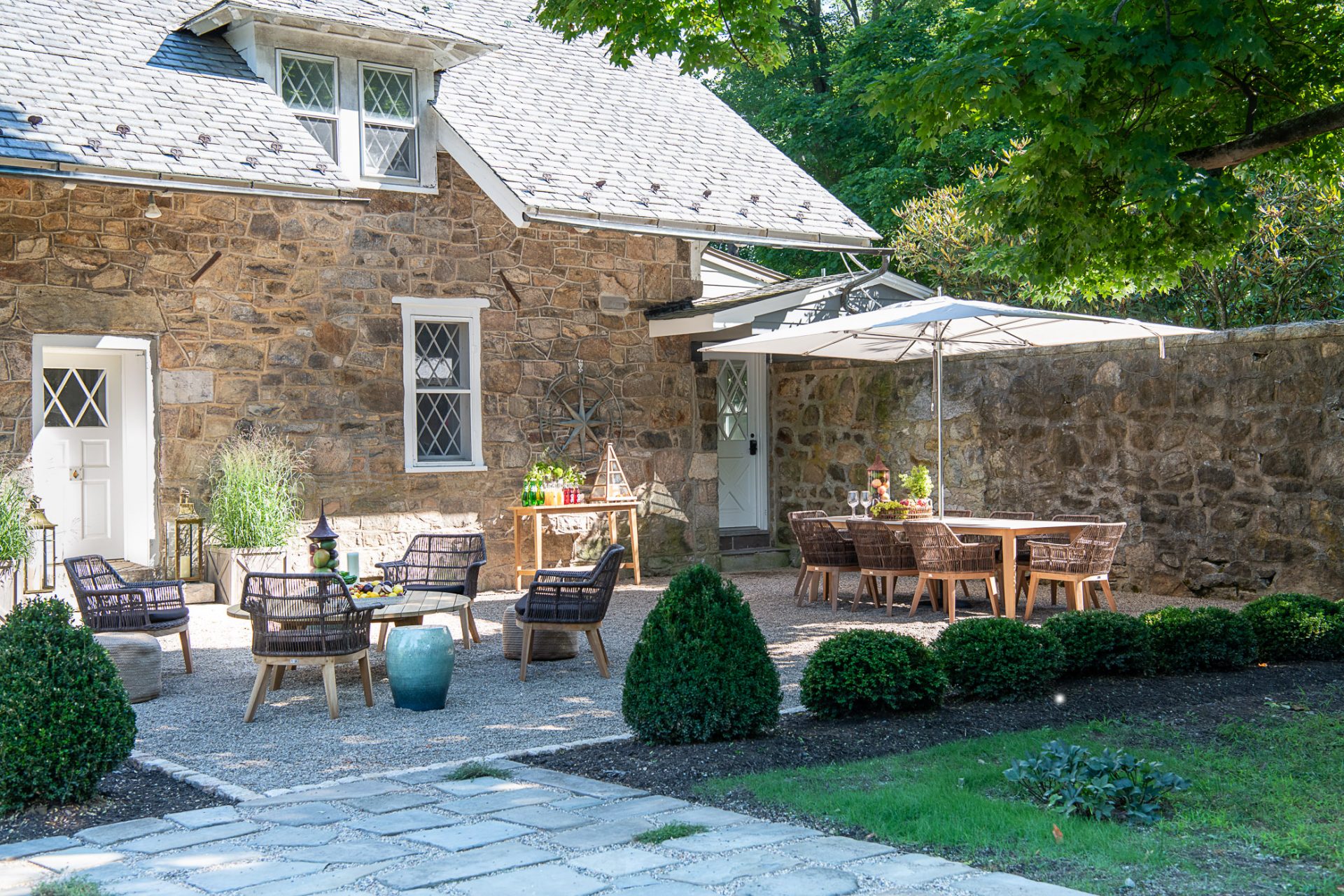 Luxury outdoor living space design featuring a gravel patio, upscale patio furniture, and a large dining table next to a historic stone home in Northern New Jersey.
