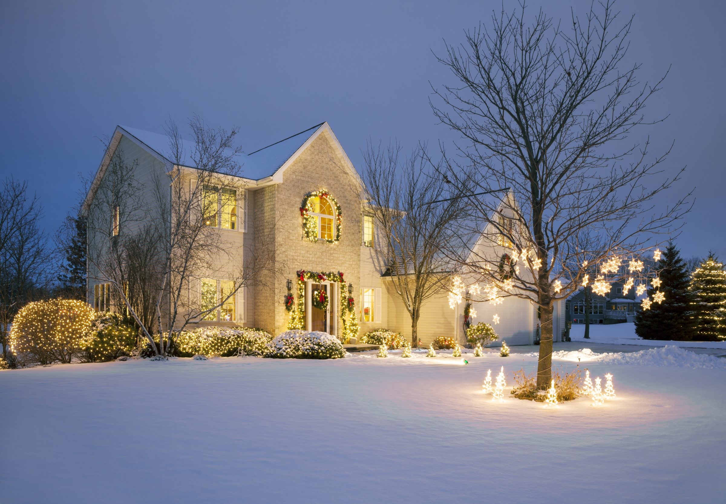 Festively lit house with snow-covered yard