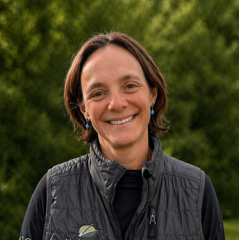 Smiling woman in vest outdoors with greenery