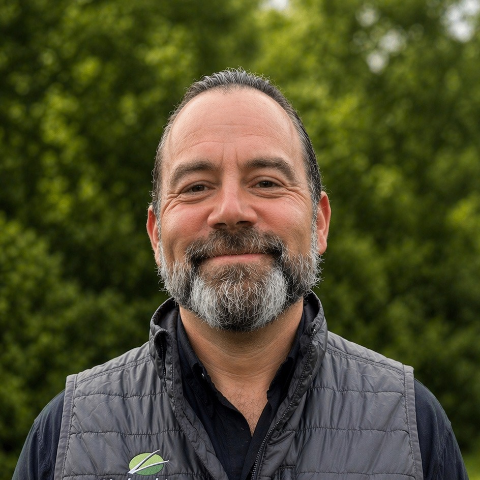 Smiling bearded man outdoors with green foliage background